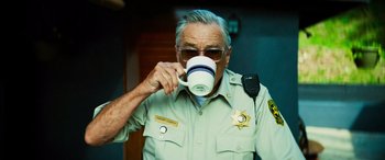 Movie still from “Savage Salvation” (2022), directed by Randall Emmett – An older man drinking from a coffee cup; Medium shot, Over the shoulder angle
