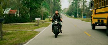 Movie still from “Savage Salvation” (2022), directed by Randall Emmett – A man riding on the back of a motorcycle down a road; Wide shot, High angle