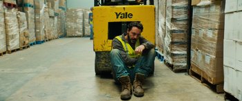 Movie still from “Savage Salvation” (2022), directed by Randall Emmett – A man sitting on the ground next to a forklift; Medium shot, High angle