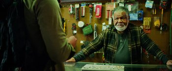 Movie still from “Savage Salvation” (2022), directed by Randall Emmett – An older man is shaking hands with a customer; Medium shot, Over the shoulder angle