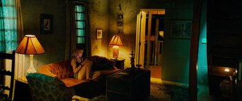 Movie still from “Savage Salvation” (2022), directed by Randall Emmett – A woman sitting on a couch looking at a book; Wide shot, High angle