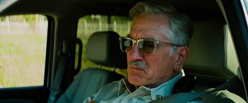 Movie still from “Savage Salvation” (2022), directed by Randall Emmett – An older man wearing glasses sitting in a car; Close Up shot, Low angle