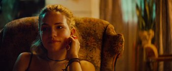 Movie still from “Savage Salvation” (2022), directed by Randall Emmett – A woman sitting in a chair with her hand on her ear; Close Up shot, Over the shoulder angle