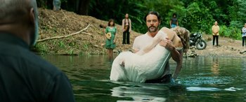 Movie still from “Savage Salvation” (2022), directed by Randall Emmett – A man holding a woman in a body of water; Medium shot, High angle