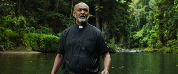 Movie still from “Savage Salvation” (2022), directed by Randall Emmett – A man wearing a priest's collar standing in a river; Medium shot, Low angle