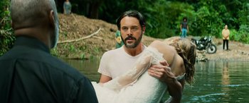 Movie still from “Savage Salvation” (2022), directed by Randall Emmett – A man and a woman in a white wedding dress by a body of water; Medium shot, Over the shoulder angle