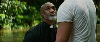 Movie still from “Savage Salvation” (2022), directed by Randall Emmett – A man wearing a priest's outfit looking into the distance; Close Up shot, Over the shoulder angle