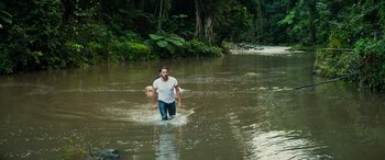 Movie still from “Savage Salvation” (2022), directed by Randall Emmett – A man and a dog are wading through a river; Wide shot, High angle