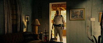 Movie still from “Savage Salvation” (2022), directed by Randall Emmett – A police officer standing at the entrance of a house; Wide shot, Low angle