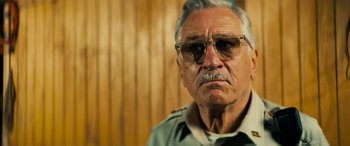 Movie still from “Savage Salvation” (2022), directed by Randall Emmett – An older man wearing glasses and a green shirt; Close Up shot, Low angle