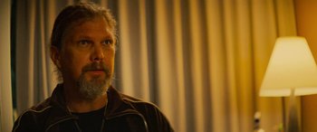 Movie still from “Savage Salvation” (2022), directed by Randall Emmett – A man with a beard is standing in front of a curtain; Close Up shot, Low angle