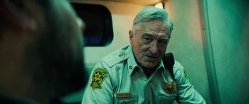 Movie still from “Savage Salvation” (2022), directed by Randall Emmett – An older police officer is sitting on a train; Close Up shot, Over the shoulder angle