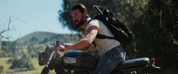 Movie still from “Savage Salvation” (2022), directed by Randall Emmett – A man on a motorcycle with a large backpack; Medium shot, Low angle