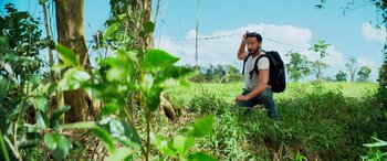 Movie still from “Savage Salvation” (2022), directed by Randall Emmett – A man with a backpack is crouching in the grass; Medium shot, Low angle