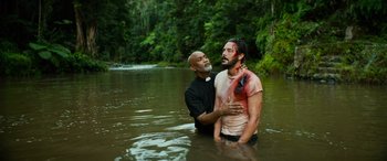 Movie still from “Savage Salvation” (2022), directed by Randall Emmett – A priest is baptizing a man in a river; Medium shot, Over the shoulder angle