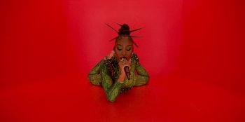 Movie still from “Savage x Fenty Show Vol. 3” (2021), directed by Alex Rudzinski – A woman in a green outfit is holding a microphone; Medium shot, Overhead angle