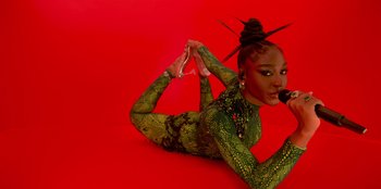 Movie still from “Savage x Fenty Show Vol. 3” (2021), directed by Alex Rudzinski – A woman in a green bodysuit is holding a microphone; Medium shot, Overhead angle