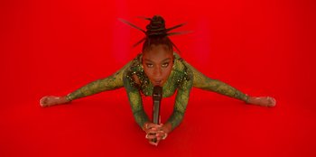 Movie still from “Savage x Fenty Show Vol. 3” (2021), directed by Alex Rudzinski – A woman in a green costume is holding a microphone; Medium shot, Overhead angle