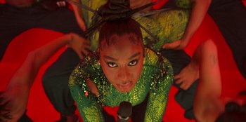 Movie still from “Savage x Fenty Show Vol. 3” (2021), directed by Alex Rudzinski – A woman in a green and yellow outfit is holding a microphone in her hand; Extreme Close Up shot, Overhead angle