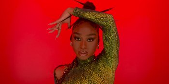 Movie still from “Savage x Fenty Show Vol. 3” (2021), directed by Alex Rudzinski – A woman in a yellow and green outfit is holding her hands up; Close Up shot, Overhead angle
