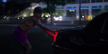Movie still from “Savage x Fenty Show Vol. 3” (2021), directed by Alex Rudzinski – A woman in a red shirt is pulling on the hood of a black car; Medium shot, High angle
