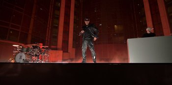 Movie still from “Savage x Fenty Show Vol. 3” (2021), directed by Alex Rudzinski – A man standing on top of a stage holding a microphone; Wide shot, Low angle