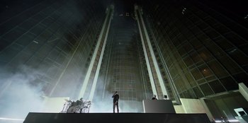 Movie still from “Savage x Fenty Show Vol. 3” (2021), directed by Alex Rudzinski – A man standing on top of a stage in front of a building; Extreme Wide shot, Low angle