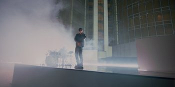 Movie still from “Savage x Fenty Show Vol. 3” (2021), directed by Alex Rudzinski – A man standing on a skateboard in front of a building; Wide shot, Low angle