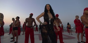 Movie still from “Savage x Fenty Show Vol. 3” (2021), directed by Alex Rudzinski – A woman in a see through dress standing in front of a group of men; Medium shot, Low angle