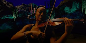 Movie still from “Savage x Fenty Show Vol. 4” (2022), directed by Alex Rudzinski – A woman is playing a violin in front of some cactus; Medium shot, Low angle