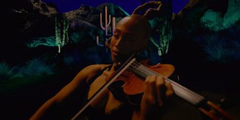 Movie still from “Savage x Fenty Show Vol. 4” (2022), directed by Alex Rudzinski – A woman playing the violin in front of a cactus background; Medium shot, Low angle