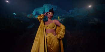 Movie still from “Savage x Fenty Show Vol. 4” (2022), directed by Alex Rudzinski – A woman in a yellow outfit standing in front of a rock formation; Extreme Wide shot, Low angle