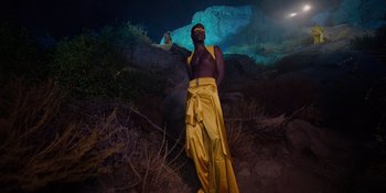 Movie still from “Savage x Fenty Show Vol. 4” (2022), directed by Alex Rudzinski – A man standing in a cave holding a bottle; Wide shot, Low angle