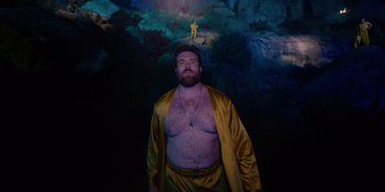 Movie still from “Savage x Fenty Show Vol. 4” (2022), directed by Alex Rudzinski – A man in a yellow robe standing in front of a cave; Wide shot, Low angle