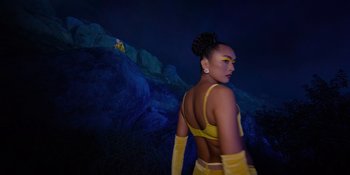 Movie still from “Savage x Fenty Show Vol. 4” (2022), directed by Alex Rudzinski – A woman in a yellow outfit standing in front of some rocks at night; Medium shot, Low angle
