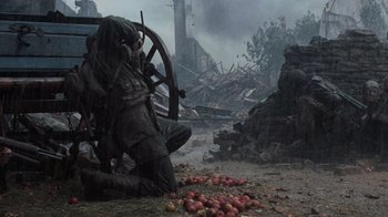 Movie still from “Saving Private Ryan” (1998), directed by Steven Spielberg – A man sitting on top of a pile of rotten apples; Wide shot, Low angle