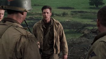 Movie still from “Saving Private Ryan” (1998), directed by Steven Spielberg – A man standing next to another man on a field; Medium shot, Over the shoulder angle