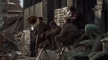 Movie still from “Saving Private Ryan” (1998), directed by Steven Spielberg – A group of men sitting on a wall; Wide shot, Low angle