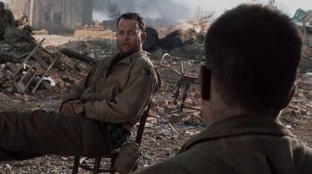 Movie still from “Saving Private Ryan” (1998), directed by Steven Spielberg – A man sitting on a chair in a field; Medium shot, Over the shoulder angle