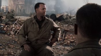 Movie still from “Saving Private Ryan” (1998), directed by Steven Spielberg – A man sitting on the ground in the middle of a field; Medium shot, Over the shoulder angle
