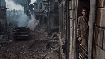 Movie still from “Saving Private Ryan” (1998), directed by Steven Spielberg – A man standing on the side of a building near buildings; Wide shot, High angle