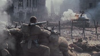 Movie still from “Saving Private Ryan” (1998), directed by Steven Spielberg – A man sitting on top of a pile of rocks; Wide shot, High angle