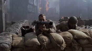 Movie still from “Saving Private Ryan” (1998), directed by Steven Spielberg – A man sitting on top of a pile of burlap bags; Medium shot, High angle