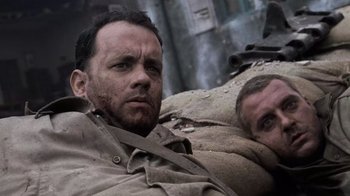Movie still from “Saving Private Ryan” (1998), directed by Steven Spielberg – A man in a trench coat is laying next to another man in a trench coat; Close Up shot, High angle