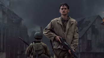 Movie still from “Saving Private Ryan” (1998), directed by Steven Spielberg – A man holding a gun while standing next to another man in fatigues; Medium shot, Low angle