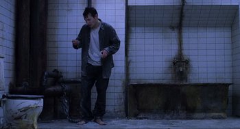 Movie still from “Saw” (2004), directed by James Wan – A man standing next to a tiled wall holding a cell phone; Wide shot, High angle