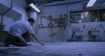 Movie still from “Saw” (2004), directed by James Wan – A man kneeling on the ground in a room; Wide shot, High angle