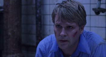 Movie still from “Saw” (2004), directed by James Wan – A person wearing a blue shirt with blood on his face; Close Up shot, Over the shoulder angle