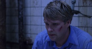 Movie still from “Saw” (2004), directed by James Wan – A man with a bruised face sitting in a room; Close Up shot, Over the shoulder angle