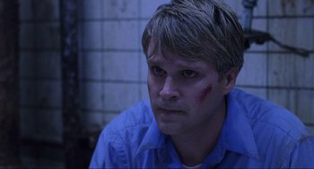 Movie still from “Saw” (2004), directed by James Wan – A person wearing a blue shirt with blood on his face; Close Up shot, Over the shoulder angle